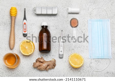 Medications for sore throat, lemons, honey, medical mask and thermometers on light background