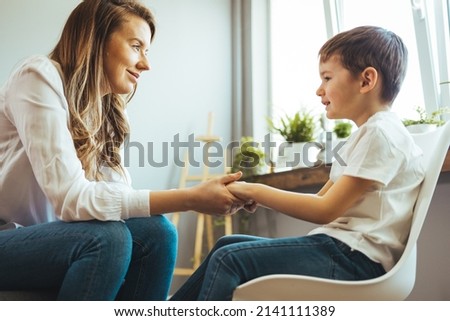 Young boy having therapy with a child psychologist. Smiling woman talking to boy. Friendly young child psychologist talking with little boy suffering from emotional disorder in bright office Royalty-Free Stock Photo #2141111389