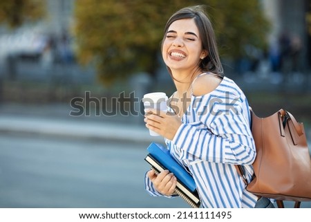 A smiling student carrying a school backpack and holding a notebook. Portrait of a happy girl in front of the school. Close-up of the face of a smiling Spanish student looking at the camera.