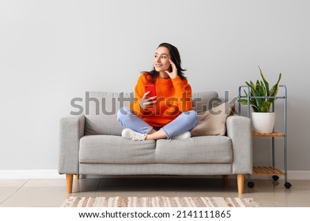 Beautiful young woman with mobile phone resting on couch at home Royalty-Free Stock Photo #2141111865