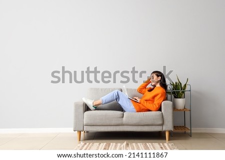 Beautiful young woman with laptop resting on couch at home