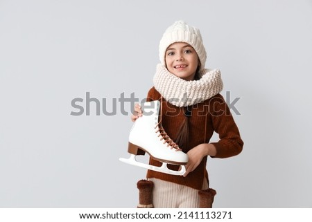 Funny little girl with ice skates on grey background