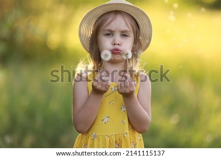 Cute little girl in a straw hat blowing on a dandelion flower on the nature in the summer. Child having activity fun outside. Concept of a healthy child without allergies. High quality photo