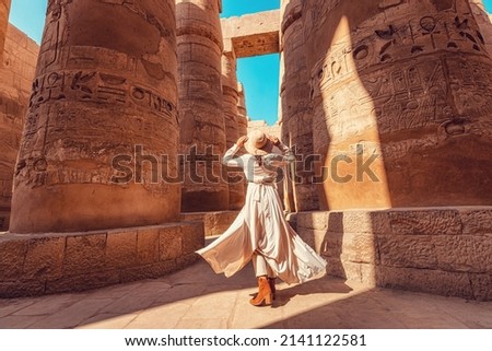 Woman traveler explores the ruins of the ancient Karnak temple in the city of Luxor in Egypt. Great row of columns with carved hieroglyph Royalty-Free Stock Photo #2141122581