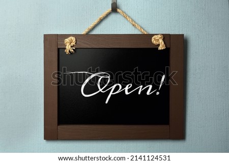 Small chalk board with word Open on light blue wall