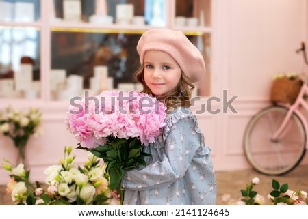 Closeup portrait of happy blonde little girl with long curly hair and in a beret with bouquet of pink peonies. Childhood concept. Celebration. cute child with flowers for mothers day. Celebration. 