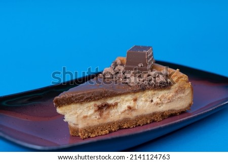 Close-up view of delicious chocolate cheesecake on purple porcelain plate shot from opposite or side angle with selective focus on isolated setting, blue background.