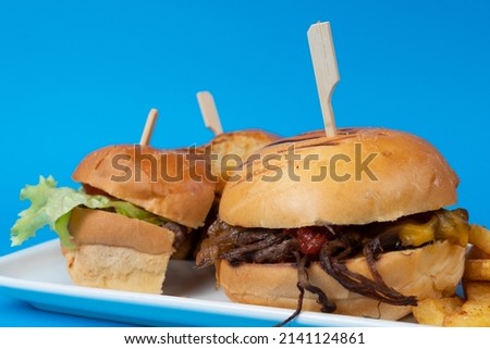 Cropped view of hamburgers on plate shot from opposite or side view with selective focus on isolated setting, blue background.