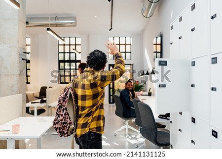 Brazilian man next to some lockers says goodbye to his co-workers before leaving the office. Royalty-Free Stock Photo #2141131125