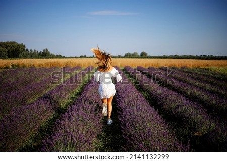 Back view of unrecognizable blonde in summer white dress walking on lavender fields 
