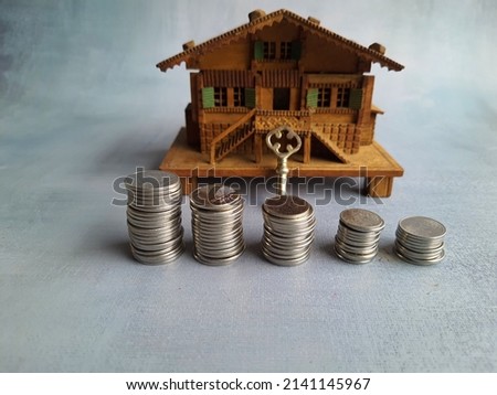 Miniature wooden house with a pile of coins, and a key kept for investment, realization of the dream of owning a home, financing, buying a property.