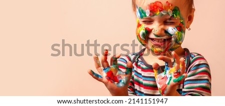 Humorous portrait of cute cheerful child girl showing her hands and face painted in bright colors. Copy space.
