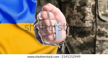 Closeup view of soldier in uniform holding military ID tag and Ukrainian flag on background. Banner design
