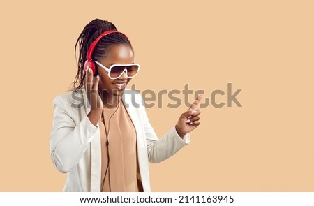 Happy young african american woman in headphones listens to music on beige background. Positive woman in sunglasses enjoys good music standing near copy space. People lifestyle concept. Banner.