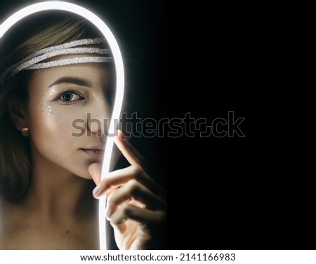The portrait of beautiful woman with shiny shimmer makeup and stars with led light stripes, neon light on black background. Futuristic style girl, sadly emotions. Future, amazing, dark night. 