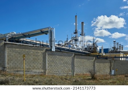 metal pipes and chimneys in a factory with concrete block wall and gas pipeline sign in the foreground