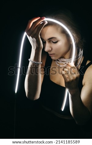 The portrait of beautiful woman with shiny shimmer makeup and stars with led light stripes, neon light on black background. Futuristic style girl, sadly emotions. Future, amazing, dark night. 