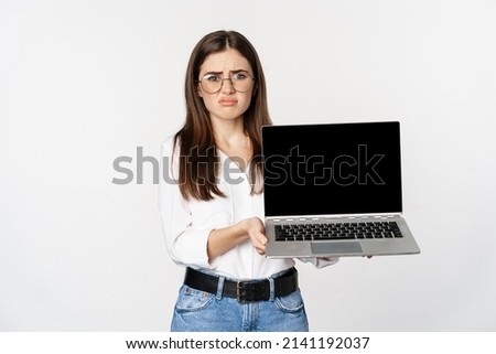 Sad brunette girl, student showing laptop screen and grimacing upset, standing disappointed against white background Royalty-Free Stock Photo #2141192037