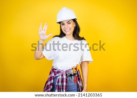 Young caucasian woman wearing hardhat and builder clothes over isolated yellow background doing hand symbol
