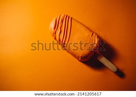 chocolate ice cream popsicle with almond flakes on orange background