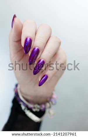 Female hand with long nails and purple plum manicure holds a bottle of nail polish