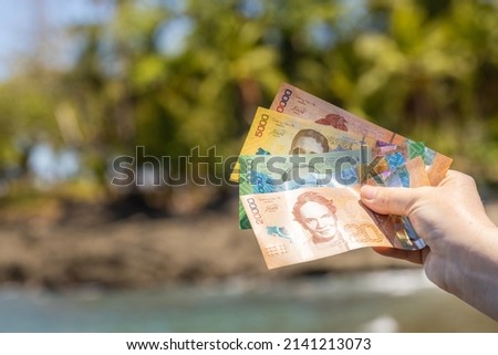 Female hand with Costa Rican money on the background of palm trees and the beach, Concept of holiday expenses, Various denominations banknotes 