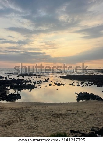 Subtle sunset over the Hawaiian coastline speckled with lava rock and sand