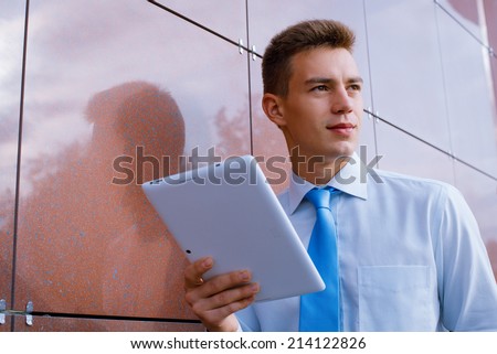 Smiling Businessman Holding Tablet Computer, Looking into the Distance,and Leaning Against Wall