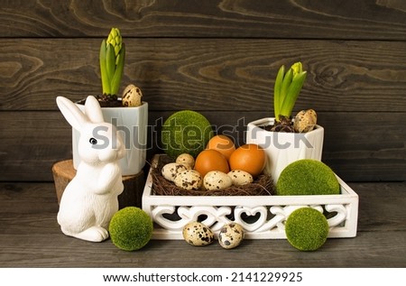 Easter decorative composition, home decoration.  On a wooden background are spring flowers, Easter eggs, a white rabbit, decorative balls of greenery.  The concept of a bright Easter holiday.