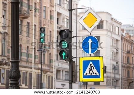 Traffic light on a pole with traffic signs: pedestrian crossing, straight ahead, main road