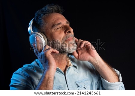 handsome bearded man in headphones listening to music. Close up portrait of cheerful mature man enjoying listening to music wearing casual jeans outfit. Happy man smiling listening to music.