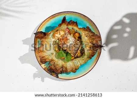 Baked halibut fillet with vegetables in parchment. Fish dish - roasted halibut with potato, broccoli and cauliflower. Food minimal concept top view. Baked white fish on white concrete background