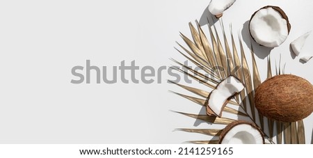 Fresh whole and broken pieces tropical coconut nut with sunny contrast shadows, gold palm leaf on light gray background top view. Creative summer food background, exotic organic healthy diet fruit Royalty-Free Stock Photo #2141259165