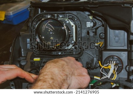 The car headlight is disassembled. Car headlight repair close-up. An auto mechanic repairs the headlight of the car. The master connects the wires in the headlight. The concept of a car service. Royalty-Free Stock Photo #2141276905
