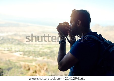 Its quite magical up here. Rear view shot of a young man taking a photo of the scenic view from the top of a mountain.