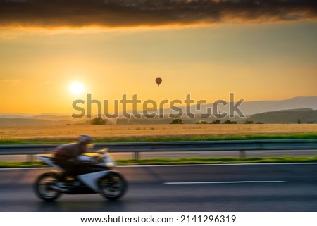 Landscape with hot air balloon and motion blurred motorcycle at sunset Royalty-Free Stock Photo #2141296319