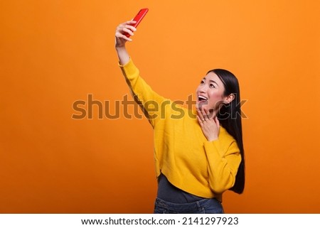 Smiling heartily pretty cute woman taking selfie photo using smartphone device to post it on social media website. Relaxed confident young adult lady photographing herself with mobile phone camera.