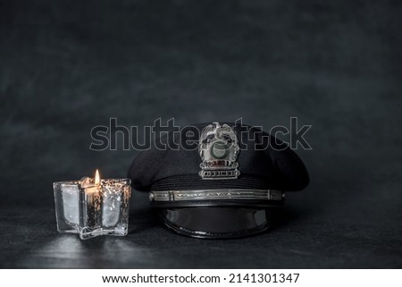 A black police hat cap in front of a navy blue background with a candle and copy space.