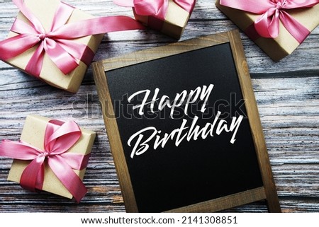 Happy Birthday text on blackboard with gift boxes on wooden background