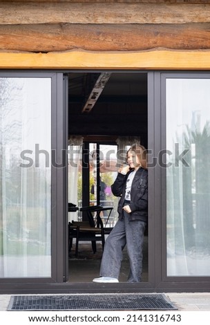 A beautiful girl with long blond hair stands in the doorway of a restaurant with a mug. Takeaway hot drink concept
