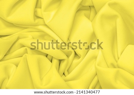 The fabric is yellow silk. Texture. Background. Pattern. Silk fabric has a shiny sheen and characteristic small folds that run horizontally. She lies down in soft folds