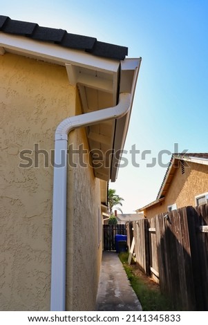 White rain gutter with downspout attached with elbow attachments.
