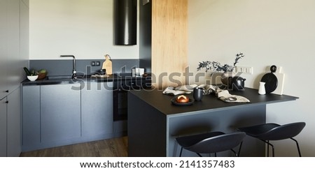 Stylish composition of modern small dining space interior. Black kitchen, kitchen island and dining accessories. Neutral walls. Minimalistic masculine concept. Details. Template.
