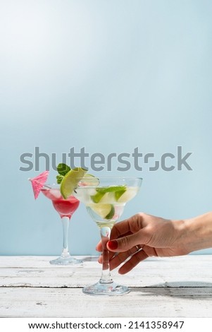 Fresh strawberry alcohol cocktail. female hand with nice red manicure holding fresh summer cocktail with strawberry, lime and ice cubes on blue background with copy space