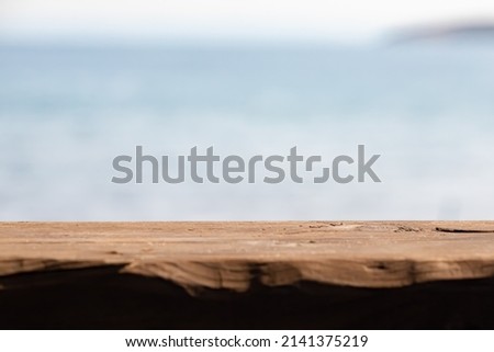 EMPTY WOODEN TABLE AGAINST THE BLUE BLURRY SEA, BEACH RESTAURANT OR BAR BACKGROUND