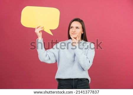 Young pretty woman is holding a yellow bubble speech while thinking. Studio shot over pink background.