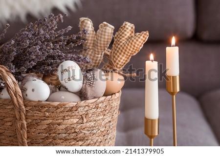 Provence. A wicker basket with Easter eggs, lavender and burning candles in the interior of the living room on a wooden table. The concept of home comfort in the bright holiday of Easter 2022. Royalty-Free Stock Photo #2141379905
