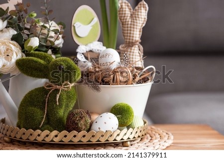 Rustic. White-green colors. Iron planters with Easter eggs, flowers, candles and rabbits in the living room interior on the table. The concept of home comfort in the bright holiday of Easter 2022. Royalty-Free Stock Photo #2141379911