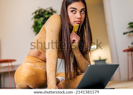 Concentrated caucasian girl, thinking what to buy using her credit card, on laptop.
