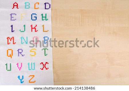 Handmade embroidered letters on white fabric, on wooden background